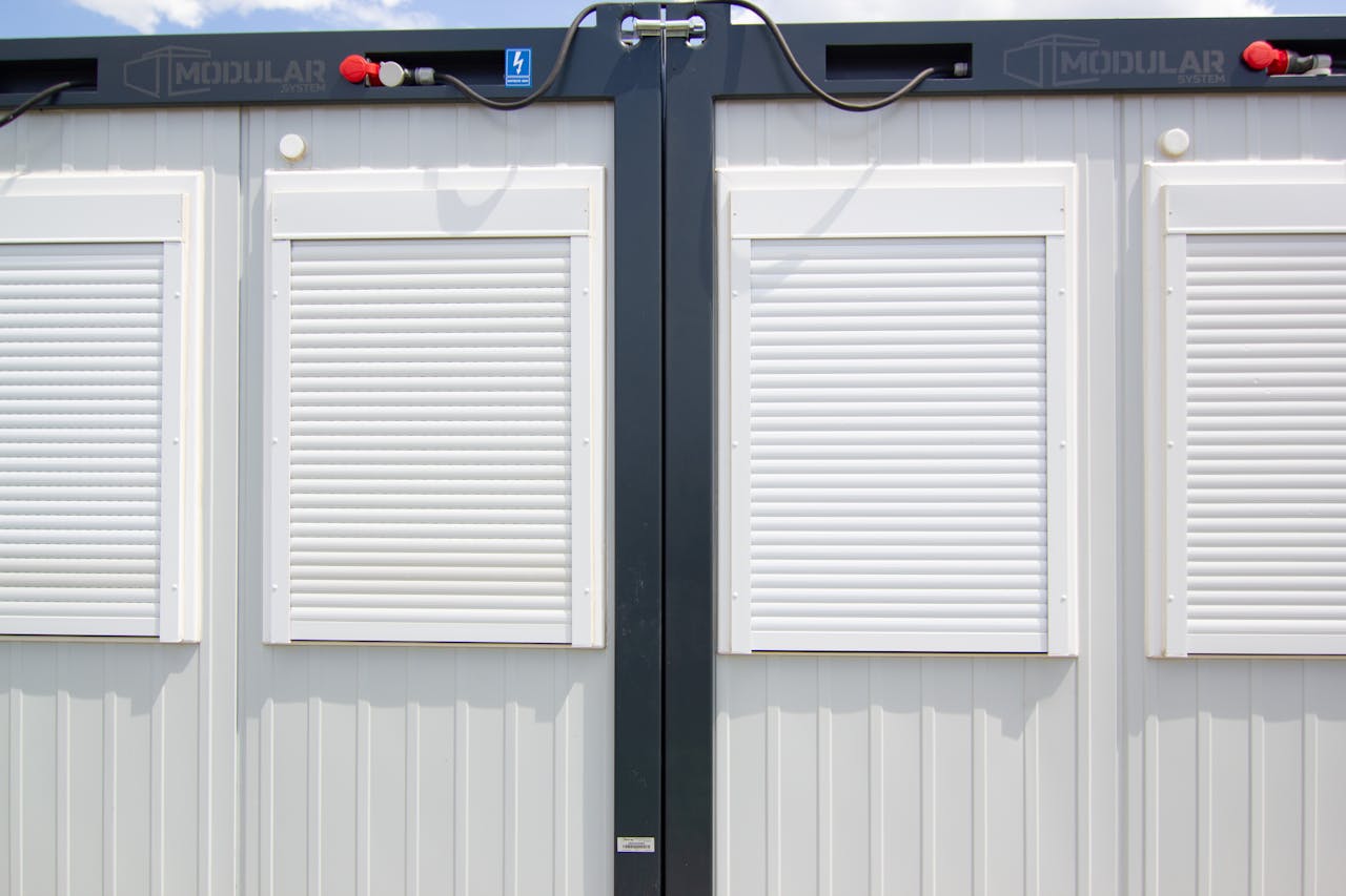 Close-up of a modular building with white shuttered windows and security features under a bright sky.
